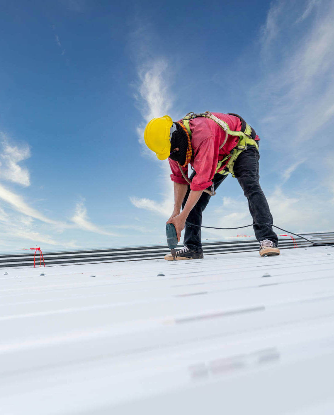 A Roofer Working On Roof Structure Of Building On Construction Site, Roofer Using Electric Drill Nail Gun And Installing White Metal Sheet On Top New Roof. Safety Body Construction