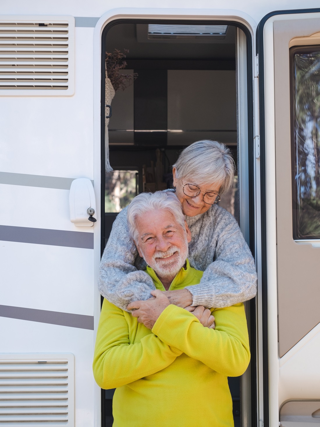 Happy Relaxed Caucasian Senior Couple Embracing On The Door Of Their Camper Van Motor Home. Smiling Attractive Elderly People Enjoying Freedom Vacation Travel In The Mountain.
